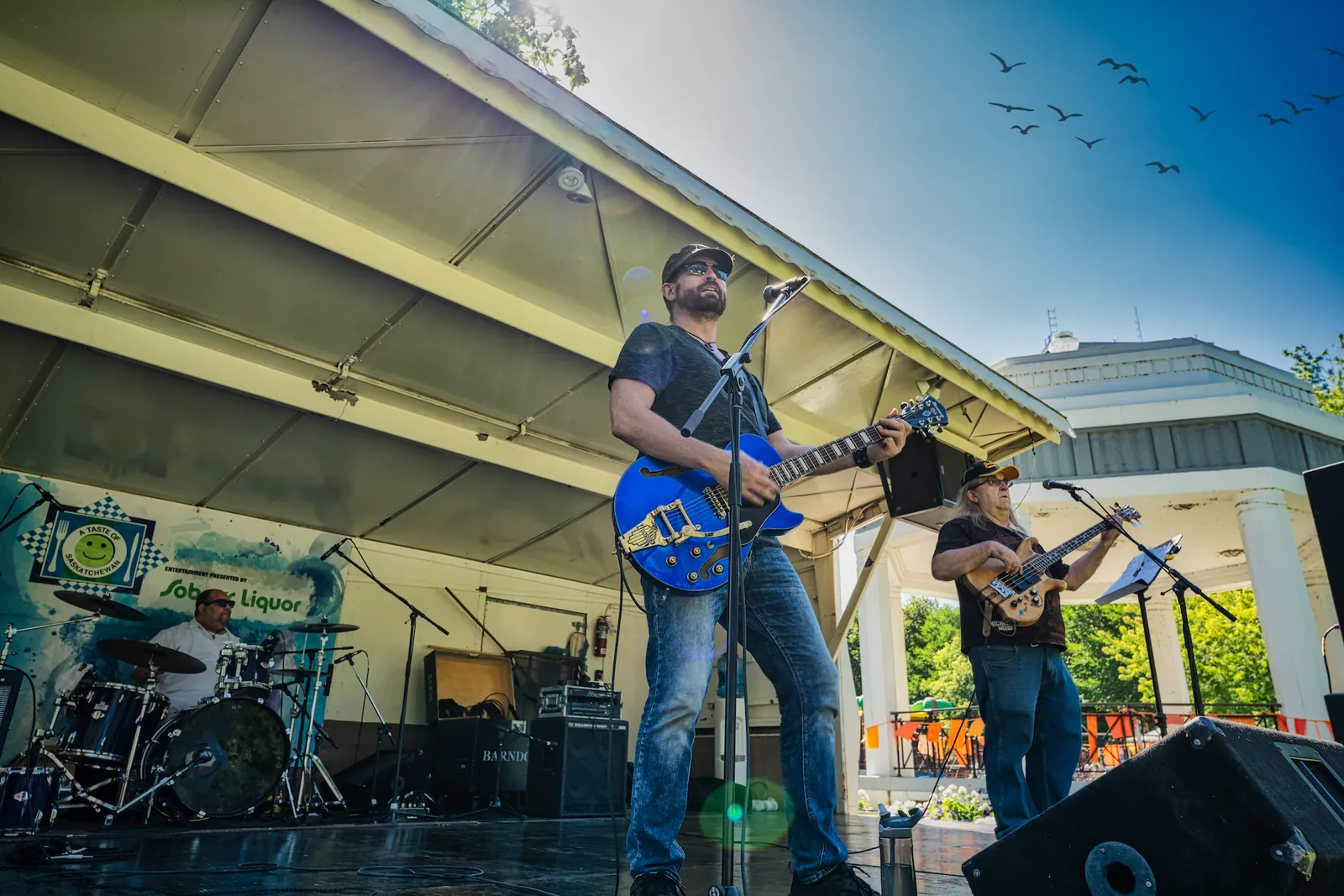 Michael Lander playing a blue electric guitar with his bassist and drummer on an outdoor festival stage